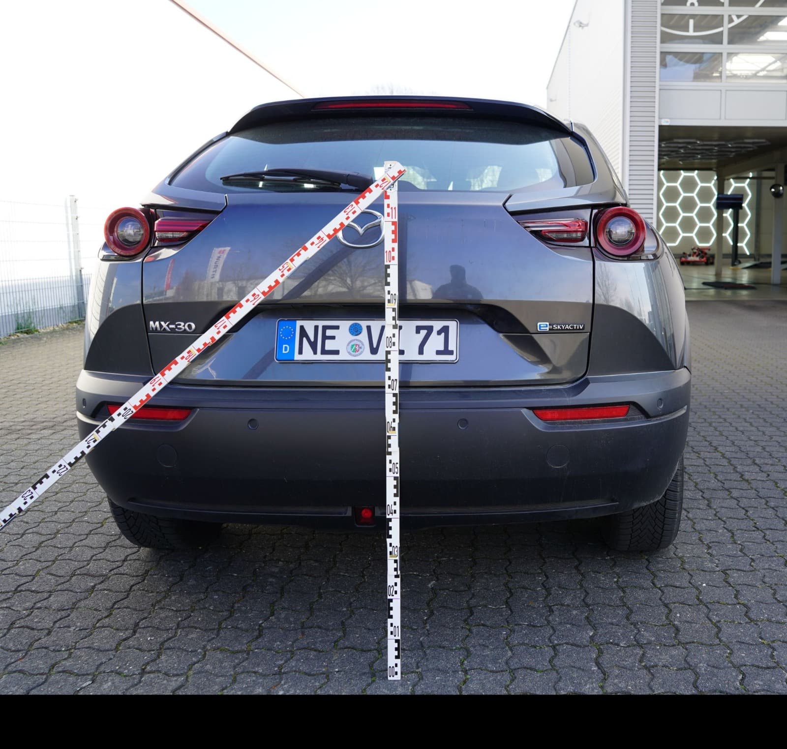 Heckansicht eines grauen Mazda MX-30 mit Messskala bei der Schadenaufnahme durch einen Gutachter in NRW.