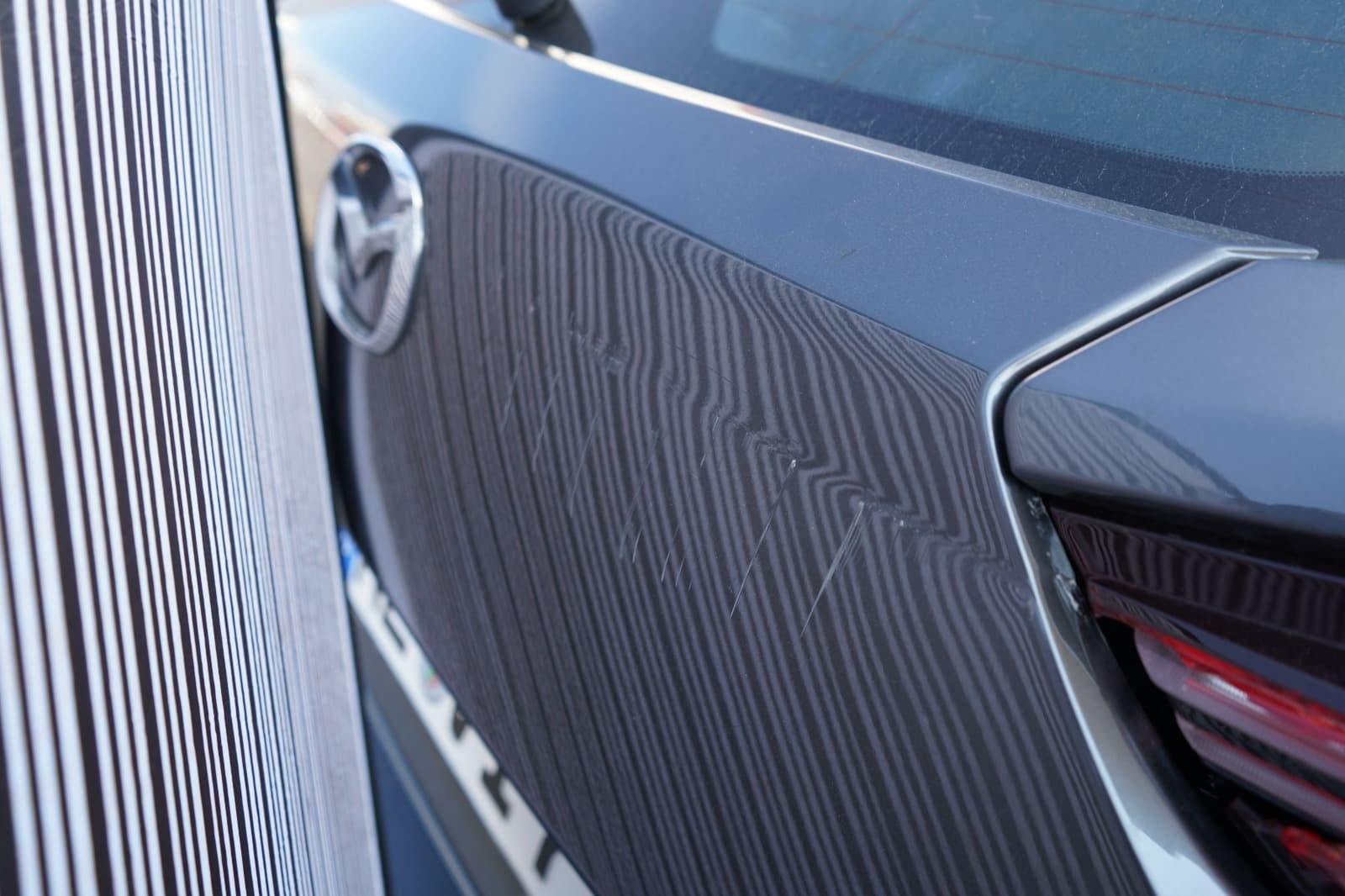 Nahaufnahme von Lack- und Karosseriespuren am Heck eines grauen Mazda MX-30.