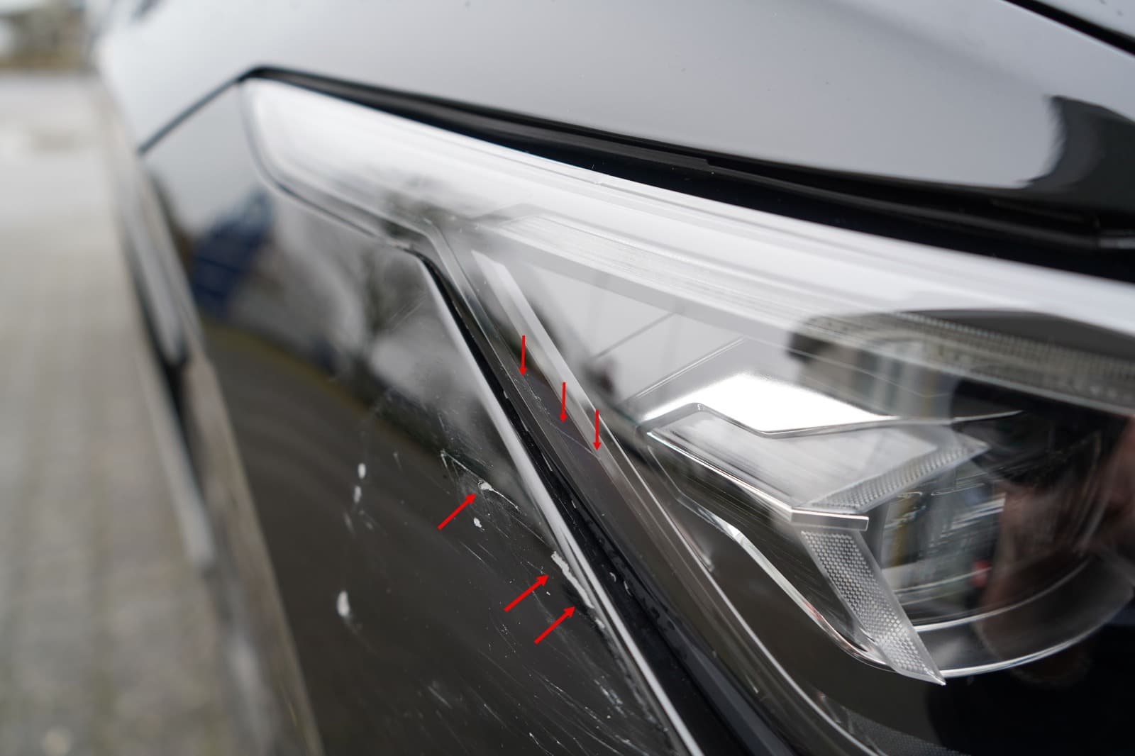 Detailaufnahme markierter Kratzer am Scheinwerferbereich eines schwarzen VW Golf.