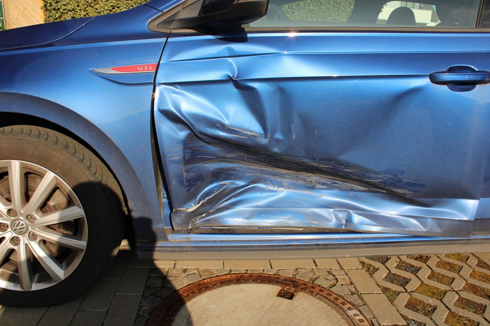 Seitenansicht eines blauen VW Polo mit deutlich sichtbarem Tur- und Seitenschaden.