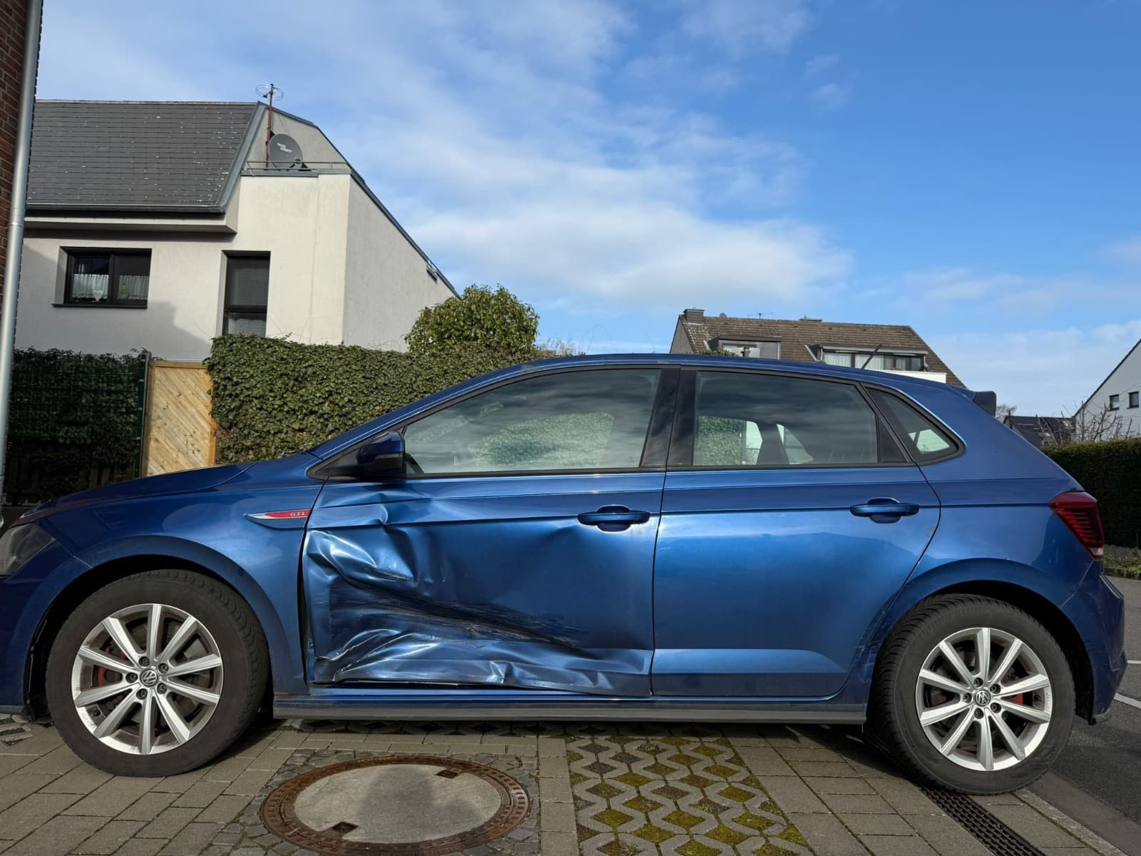 Seitenansicht eines blauen VW Polo mit Messskala zur Dokumentation des Unfallschadens.