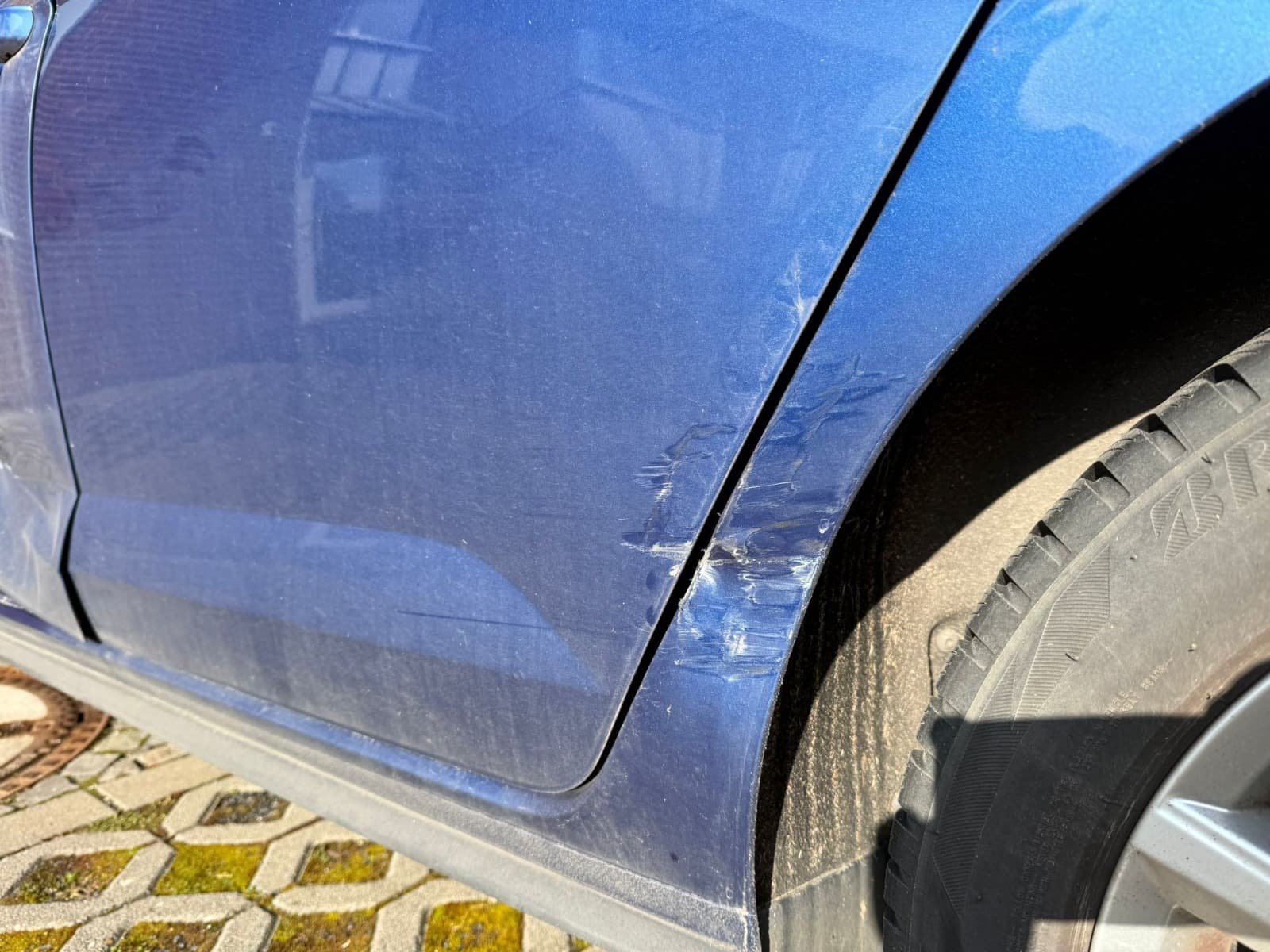 Nahaufnahme eines markierten Seitenschadens am blauen VW Polo im Bereich Radlauf und Tur.